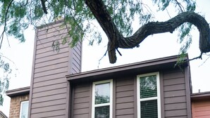 A two-story house with a green door, a brick chimney, and a small garden area with plants and a pathway. - Beautiful family-friendly 3-bedroom townhome in Corpus Christi (Corpus Christi)
