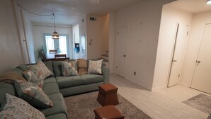 A living room with a sectional sofa, two ottomans, a rug, and a staircase leading to another room. - Beautiful family-friendly 3-bedroom townhome in Corpus Christi (Corpus Christi)