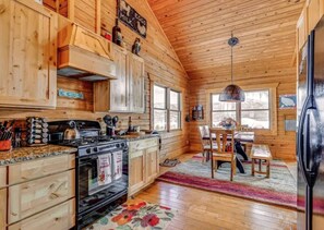 A wooden cabin interior with a kitchen, dining area, and a refrigerator. - Private Hot Tub: Mtn-View Grand Lake Cabin! (Grand Lake)