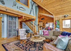 A cozy cabin interior with a wooden staircase, a leather chair, a patterned rug, and a couch with pillows. - Private Hot Tub: Mtn-View Grand Lake Cabin! (Grand Lake)
