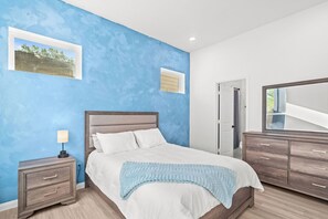 Quarto com cama, mesa de cabeceira, cômoda e janela com vista.