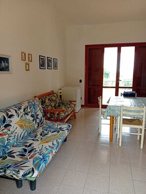 A living room with a sofa, a dining table with chairs, a refrigerator, and a door leading outside. - Vacation home with garden in Torre dei Corsari (Torre dei Corsari)