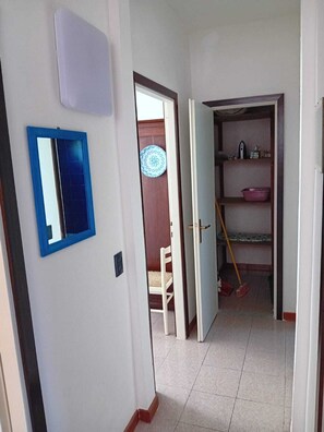 A hallway with a blue-framed mirror, a white door, and a room with a bed, a chair, and a shelf with items. - Vacation home with garden in Torre dei Corsari (Torre dei Corsari)