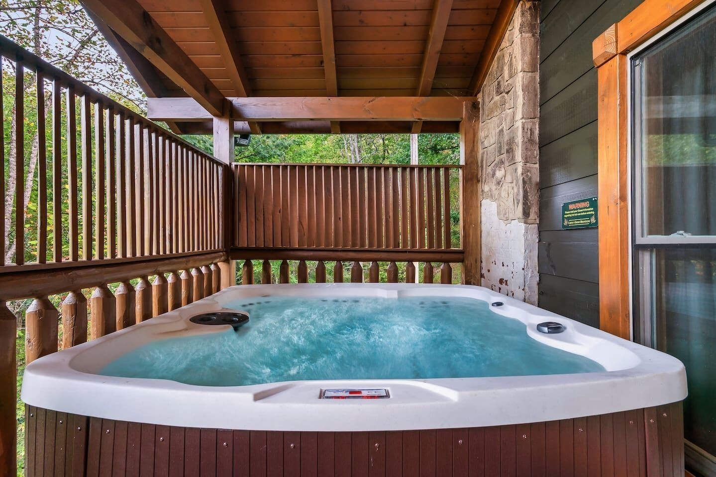 A hot tub in an outdoor wooden deck area with a wooden railing and a stone wall.