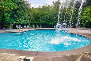 A swimming pool with a water feature, surrounded by lounge chairs and a stone deck. - Falcon's Rest | 5 Min to Gatlinburg | Sleeps 18 (Gatlinburg)