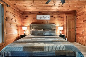 A wooden cabin bedroom with a bed, two bedside lamps, and a sign on the wall. - Falcon's Rest | 5 Min to Gatlinburg | Sleeps 18 (Gatlinburg)