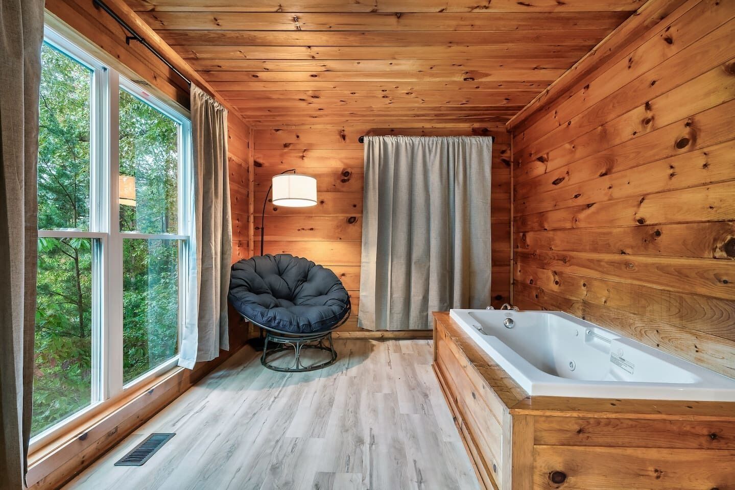 L’intérieur d’un chalet en bois, avec une grande fenêtre, un fauteuil rond et une baignoire.