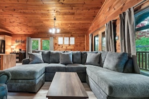 Ein gemütliches Blockhaus-Interieur mit einer großen, winkelförmigen Eckcouch, einem Holztisch und einer Holzbalkendecke.