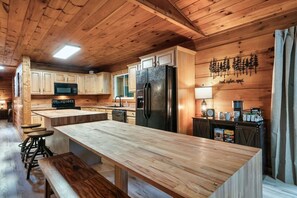 A wooden interior with a kitchen featuring a central island, bar stools, and a refrigerator. - Falcon's Rest | 5 Min to Gatlinburg | Sleeps 18 (Gatlinburg)
