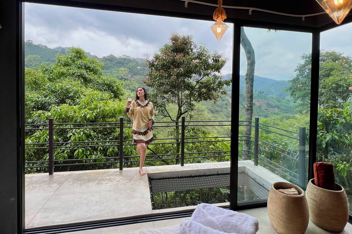 Una habitación con un ventanal grande, una cama, un balcón pequeño y vistas al verdor.