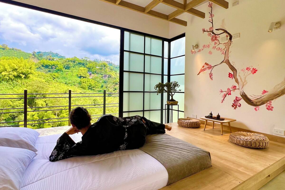 Una habitación con una cama grande, vista a zonas verdes y estructura de techo de madera.