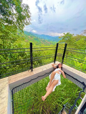 A person lying on a hammock in a lush green landscape with a view of distant hills.