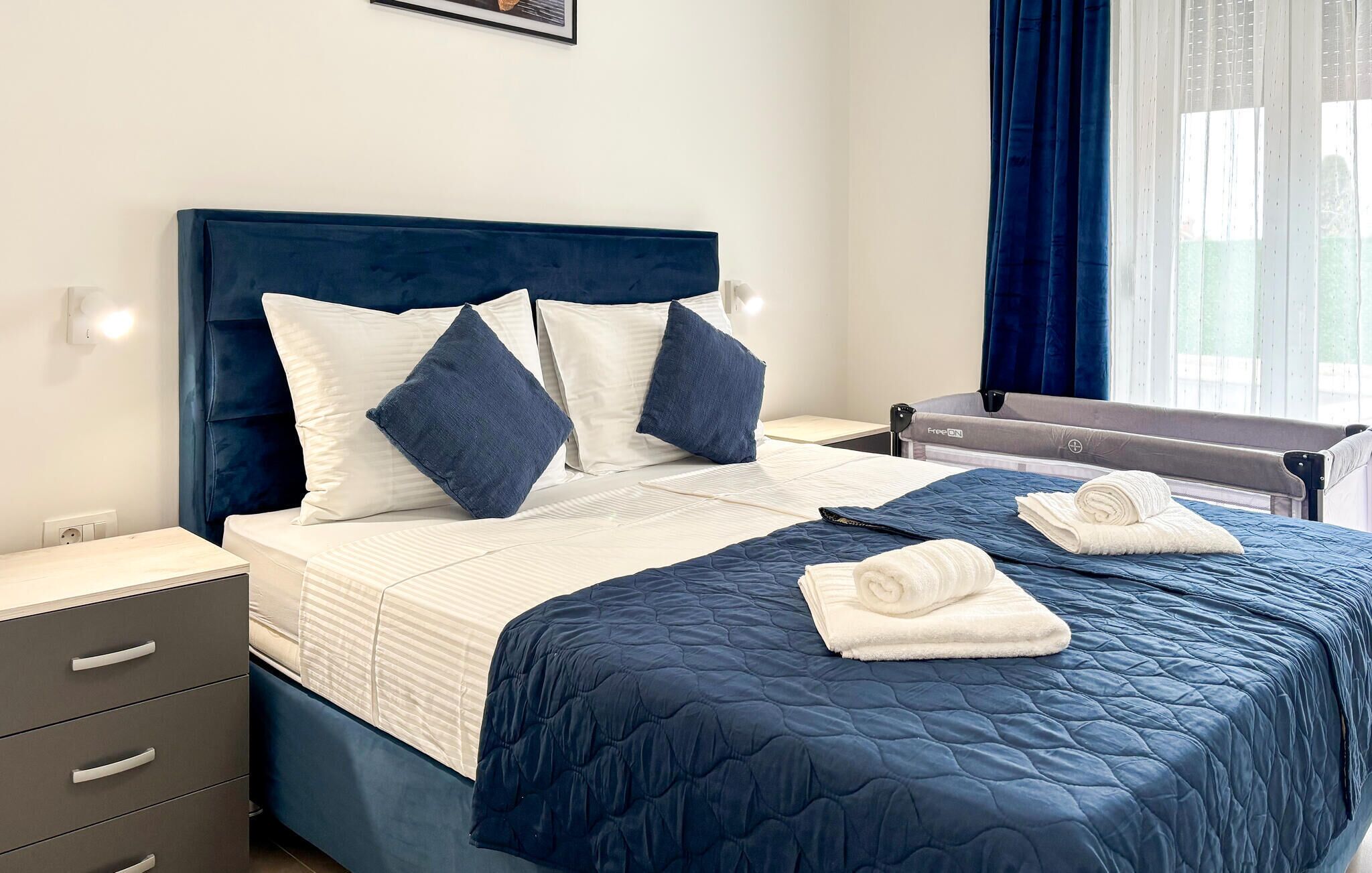 Een hotelkamer met een bed, nachtkastje, ladeblok en raam met gordijnen.