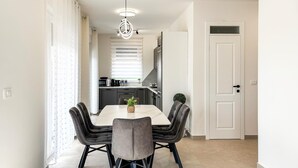 A modern kitchen with a dining area, featuring a white table, dark chairs, and a hanging light fixture. - Cozy home in Nedescina (Nedescina)