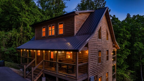A two-story log cabin with a porch and multiple windows, surrounded by trees. - The Brookshire! Premium View | Hot Tub | Top 10% (Sevierville)