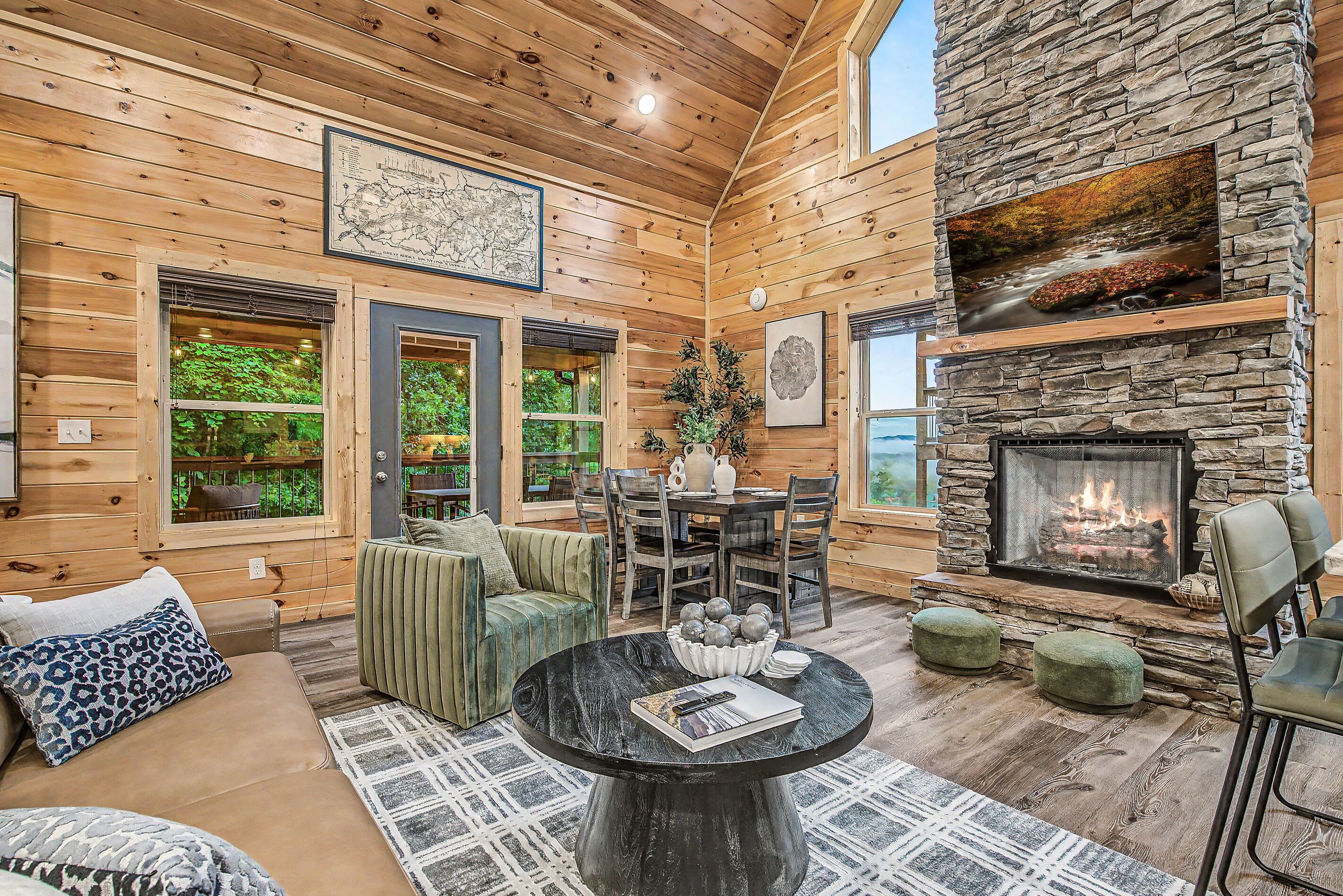 A cozy cabin interior with a stone fireplace, wooden walls, and a dining area.