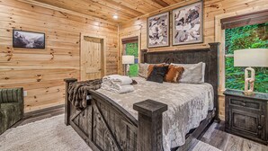 A wooden cabin interior with a bed, a ceiling fan, and framed artwork on the walls. - The Brookshire! Premium View | Hot Tub | Top 10% (Sevierville)