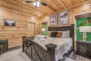 A wooden cabin interior with a bed, a ceiling fan, and framed artwork on the walls. - The Brookshire! Premium View | Hot Tub | Top 10% (Sevierville)