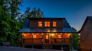 A two-story log cabin with a porch, multiple windows, and a metal roof. - The Brookshire! Premium View | Hot Tub | Top 10% (Sevierville)
