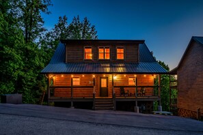 A two-story log cabin with a porch, multiple windows, and a metal roof. - The Brookshire! Premium View | Hot Tub | Top 10% (Sevierville)