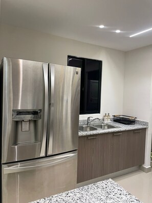 A stainless steel refrigerator with a water dispenser, a black microwave, a granite countertop, a double sink, and wooden cabinets.