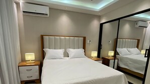 A modern bedroom with a large bed, bedside tables with lamps, a ceiling fan, and an air conditioning unit.