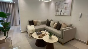 A modern living room with a sectional sofa, two round coffee tables, a hanging light fixture, and a painting on the wall.