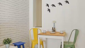 A room with a white brick wall, a wooden table with chairs, a small plant, and wall art. - Newly Furnished! 1BR/1BA in OldLisbon SaoBento (Lisboa)