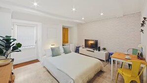 A modern bedroom with a bed, bedside table, TV, and a small dining area with a chair and table. - Newly Furnished! 1BR/1BA in OldLisbon SaoBento (Lisboa)