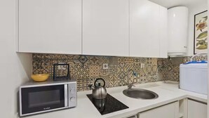 A kitchen with white cabinets, a microwave, a kettle, a sink, and patterned backsplash tiles. - Newly Furnished! 1BR/1BA in OldLisbon SaoBento (Lisboa)