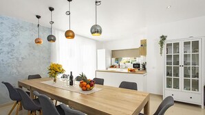 Un espace de salle à manger moderne avec une table en bois, des chaises à revêtement gris et des luminaires suspendus.