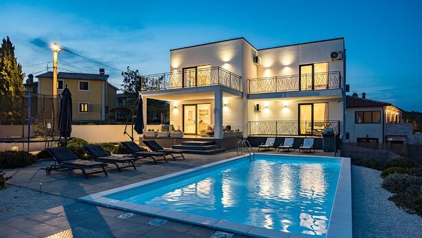 Une maison à deux étages avec une piscine, un espace salon extérieur et un balcon.