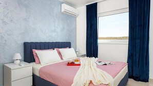 Une chambre à coucher comprenant un lit, une table de chevet, une lampe, un appareil de climatisation et une fenêtre avec des rideaux.