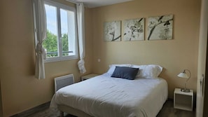 A bedroom with a bed, a window with curtains, a radiator, and wall art.