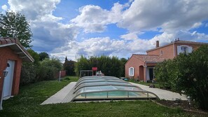 Zona residencial con una estructura de invernadero de vidrio, una casa de ladrillo rojo y cielo despejado.