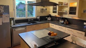 A modern kitchen with a central island, a built-in oven, and a window with a view of greenery. - Villa with pool in Toulouse - 5 bedrooms, garden, 10 travellers (Cugnaux)