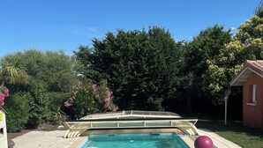 A rectangular swimming pool with a built-in ladder, surrounded by a tiled deck and a grassy area with trees and shrubs. - Villa with pool in Toulouse - 5 bedrooms, garden, 10 travellers (Cugnaux)