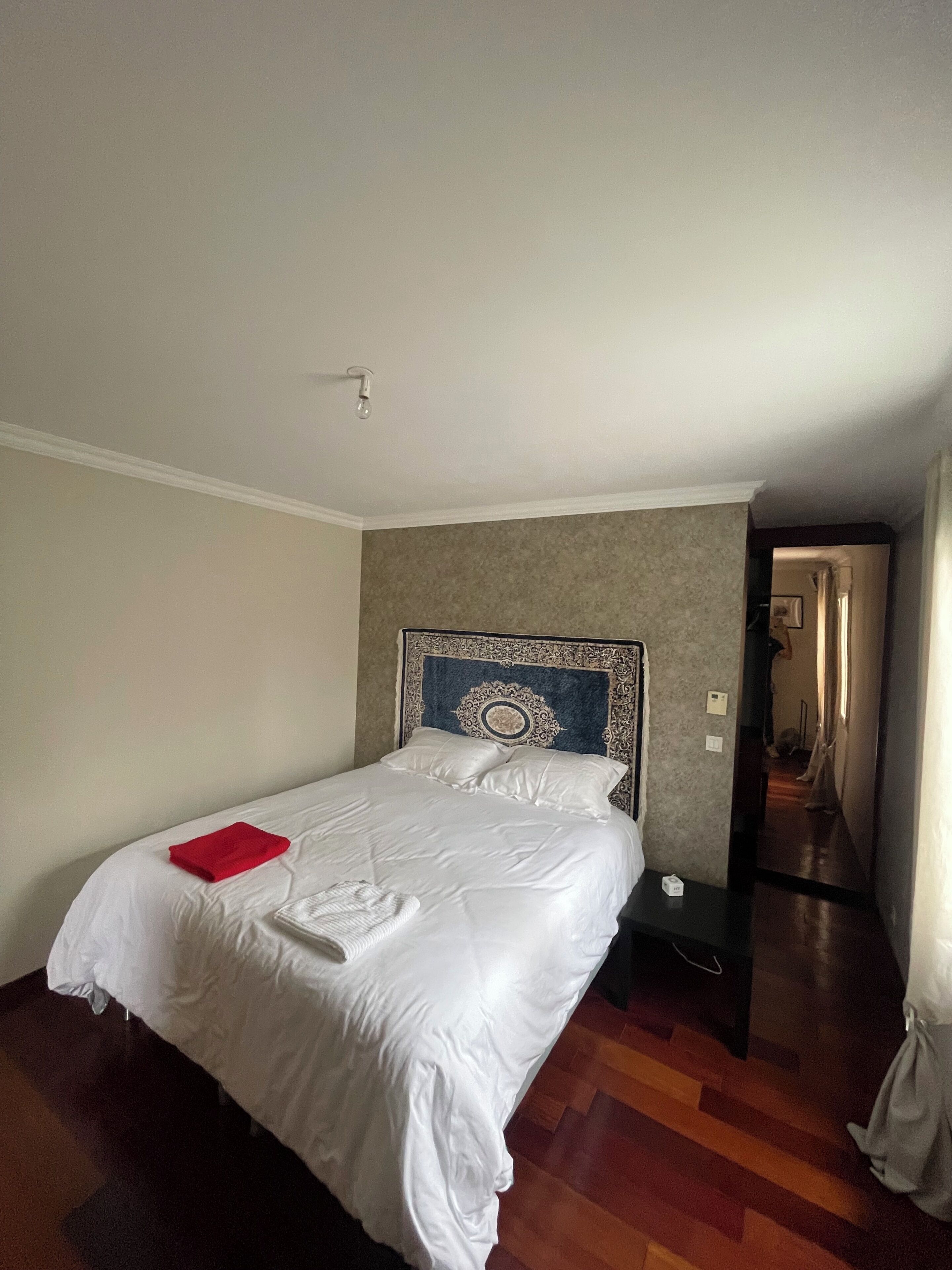 A hotel room with a bed, a nightstand, a red towel, and a wooden floor.
