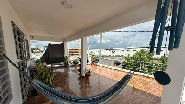 A balcony with a hammock, potted plants, and a view of buildings. - Lovely apartment with AC in vibrant Punta Cana. 10min to Beach & Downtown. (Punta Cana)