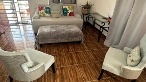 A room with a sofa, ottoman, two armchairs, a small table, and a potted plant. - Lovely apartment with AC in vibrant Punta Cana. 10min to Beach & Downtown. (Punta Cana)