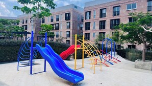 A playground with slides and climbing structures, surrounded by a brick building with multiple windows. - Ideal apartment for families, barbecue, court and children's play areas. (Oaxaca de Juárez)