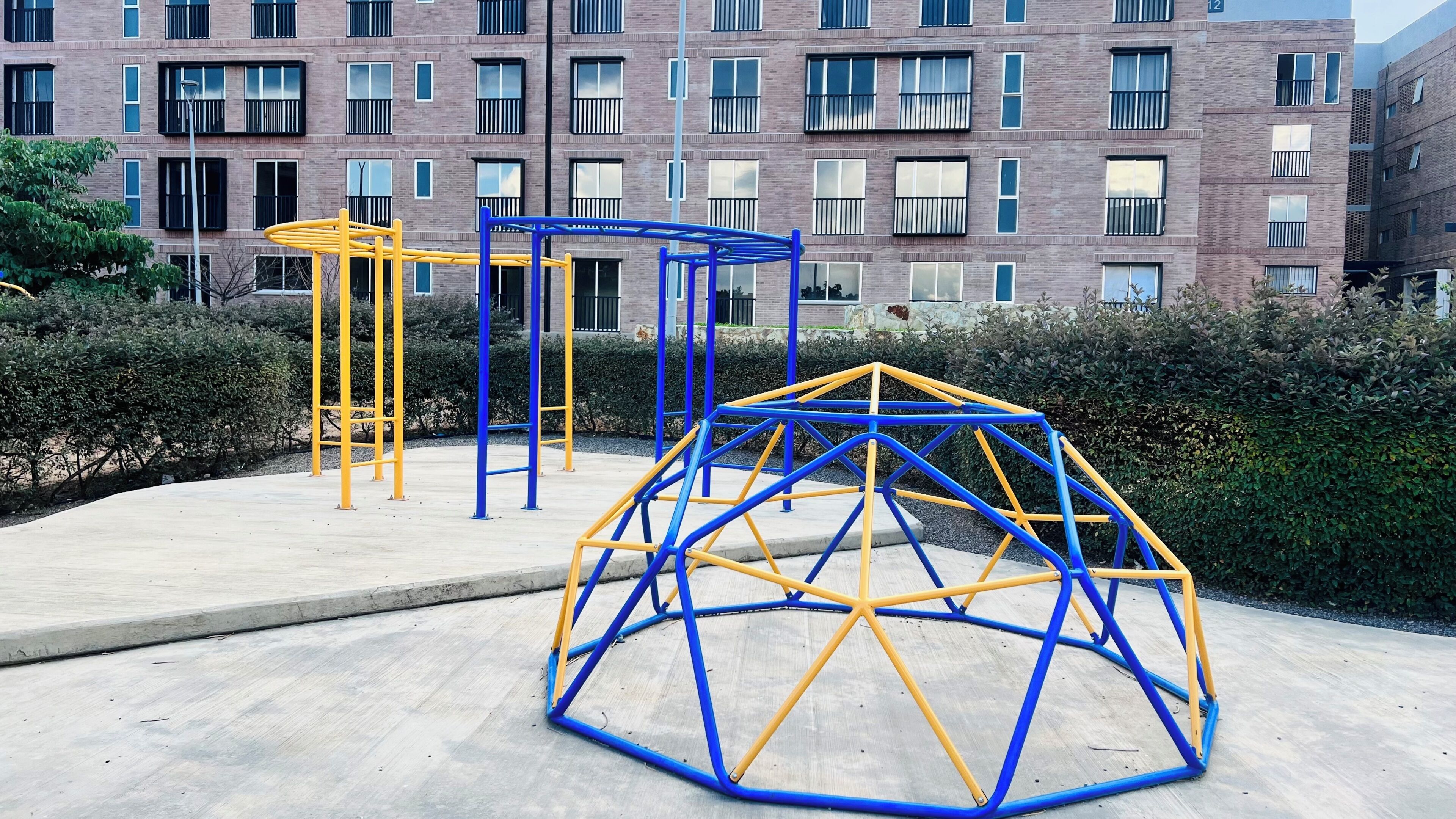 Outdoor exercise equipment, a building with multiple windows, and a hedge.
