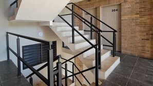 A modern staircase with black railings, a beige wall, and a brick wall in the background. - Ideal apartment for families, barbecue, court and children's play areas. (Oaxaca de Juárez)