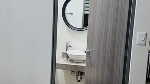 A bedroom with a bed, a bedside table, and a door leading to a bathroom with a sink and mirror. - Ideal apartment for families, barbecue, court and children's play areas. (Oaxaca de Juárez)
