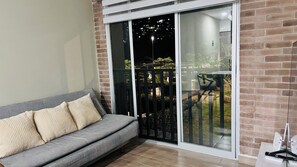 Ein Zimmer mit grauem Sofa, einer Schiebetür zu einem Balkon mit Blick auf die beleuchtete Stadt.