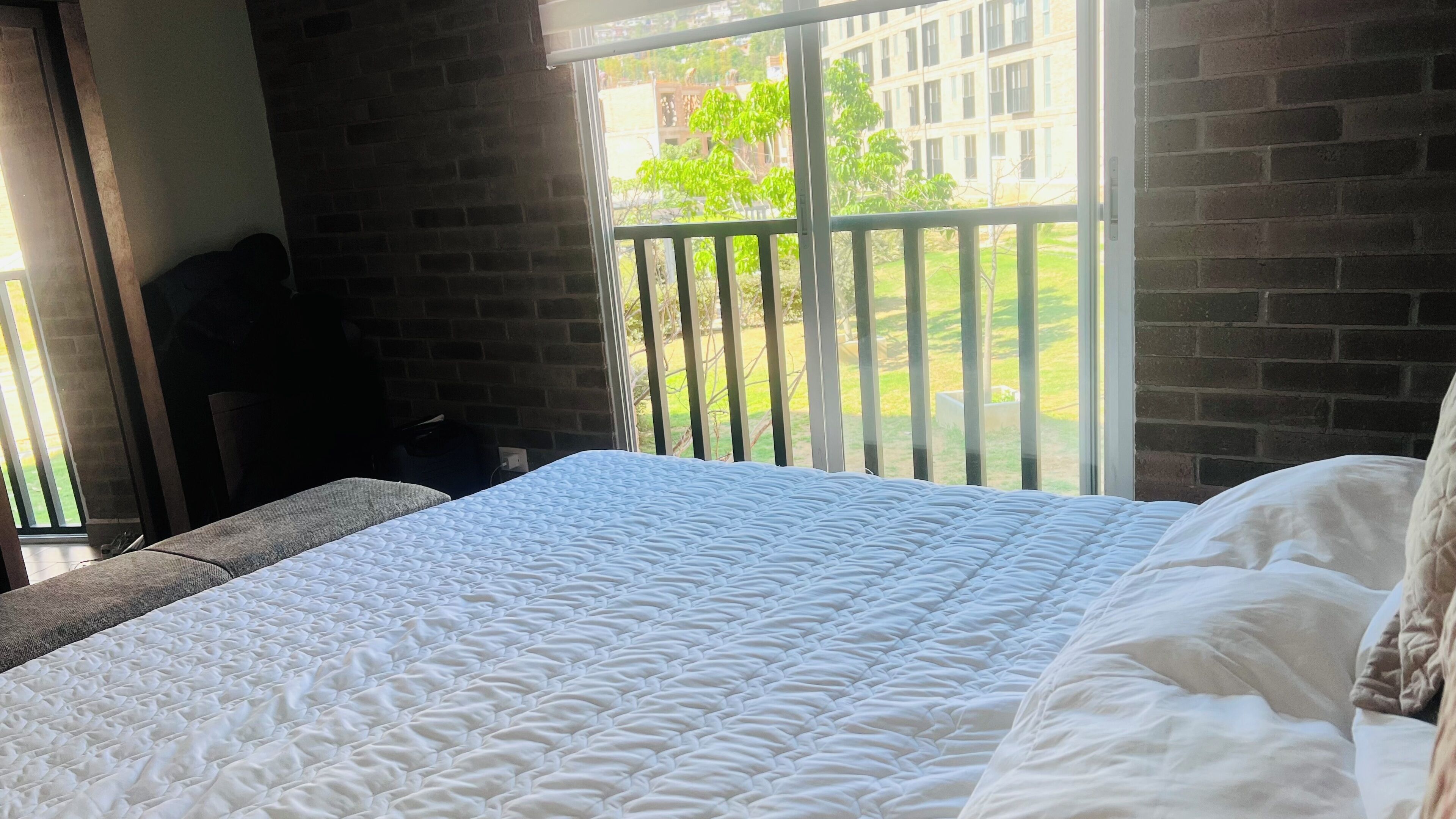 Ein Hotelzimmer mit einem großen Bett, Blick auf ein Backsteingebäude und einem Balkon mit Geländer.