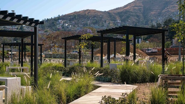 A garden area with pergolas, a concrete pathway, and a view of a hillside with houses. - Ideal apartment for families, barbecue, court and children's play areas. (Oaxaca de Juárez)