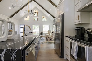 A modern kitchen with a marble countertop, stainless steel appliances, and a high ceiling with exposed beams. - NEW! Updated Secluded Cabin w/ Hot Tub, Fire Pit, Outdoor Lounge & Forest Views (Broken Bow)