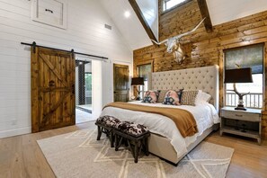 A bedroom with a large bed, wooden walls, a barn door, and a window with a view. - NEW! Updated Secluded Cabin w/ Hot Tub, Fire Pit, Outdoor Lounge & Forest Views (Broken Bow)