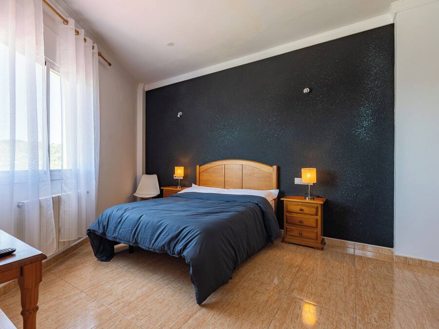 A bedroom with a bed, bedside tables, a lamp, a window with curtains, and a wall with a starry pattern.